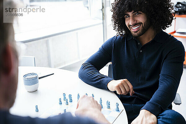 Smiling businessman playing chess with colleague at office