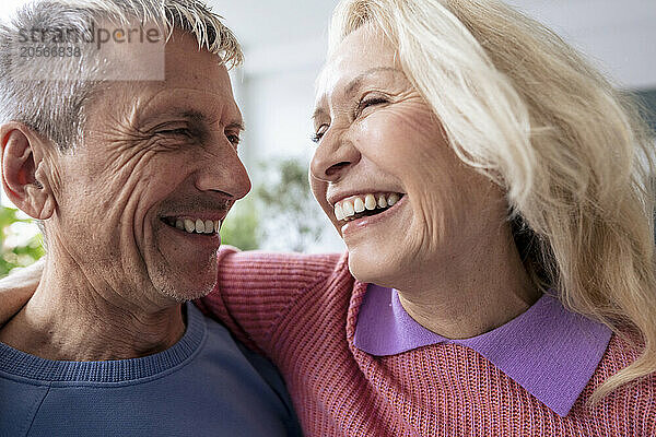 Cheerful blond senior woman with arm around man at home