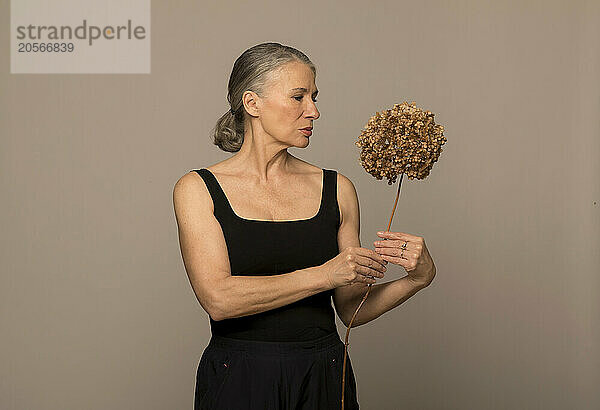 Senior woman looking at withered flower against brown background