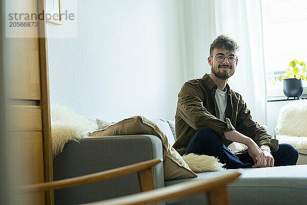 Smiling young man sitting on sofa at home