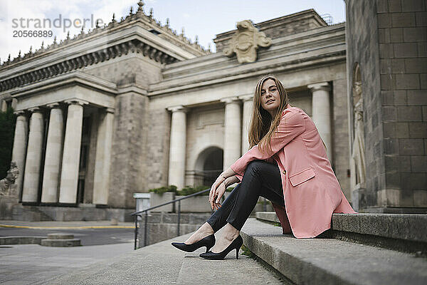 Young woman wearing pink coat sitting on stairs of Palace of Culture