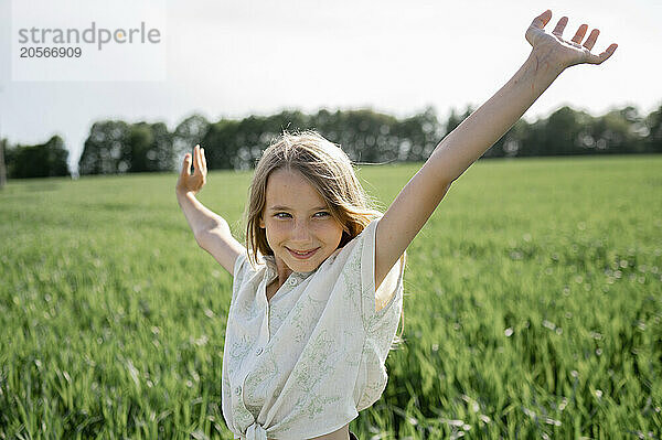 Happy girl standing with arms raised in field