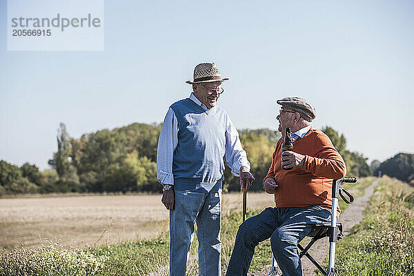 Senior men sitting on mobility walker near friend at field