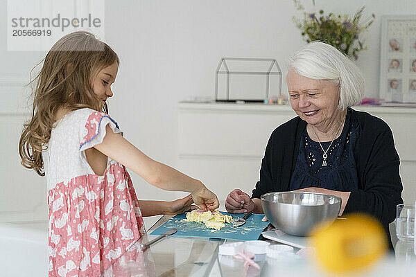 Girl kneading dough by grandmother at home