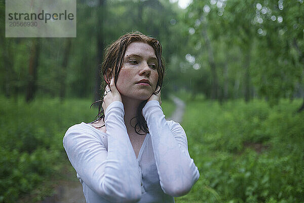 Thoughtful hipster woman in rain at forest