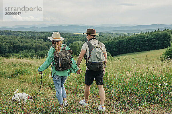 Young couple wearing backpacks and hiking with dog on mountain