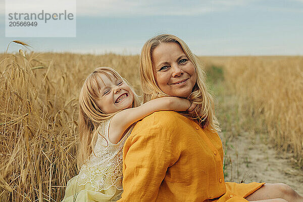 Playful girl with arm around mother at wheat field