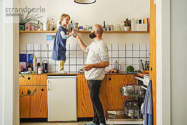 Daughter helping father holding glasses in kitchen at home