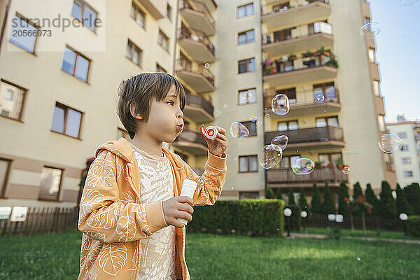 Boy blowing soap bubbles in front of buildings