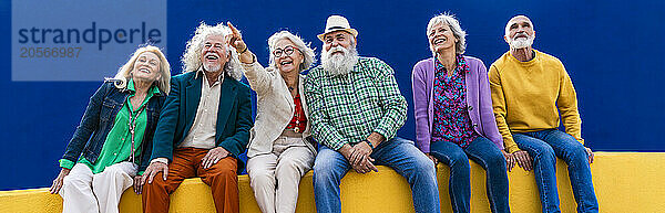 Cheerful senior friends sitting on wall