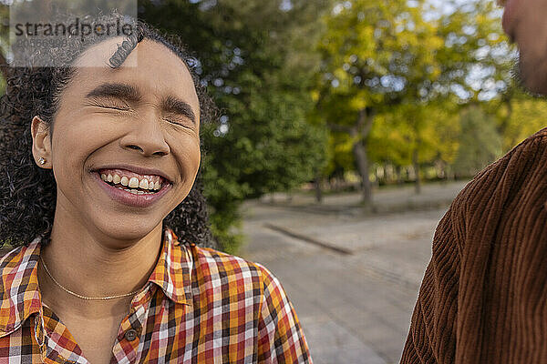 Cheerful young woman with curly hair laughing at park