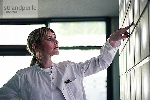 Confident female doctor pointing at wall in hospital