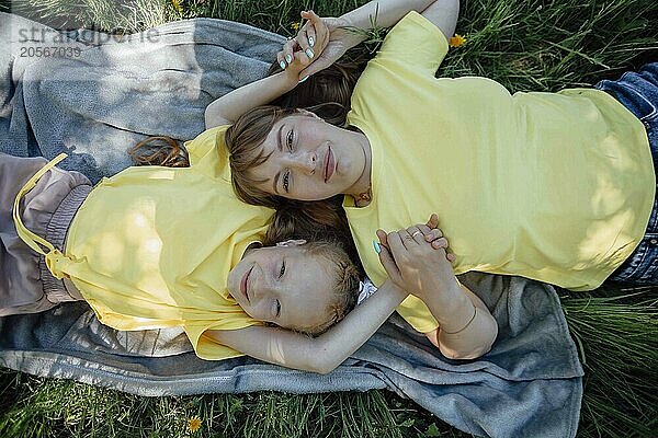 Smiling mother holding hands with daughter and lying on blanket in garden