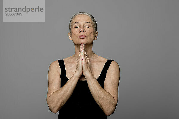 Senior woman with hands clasped against gray background