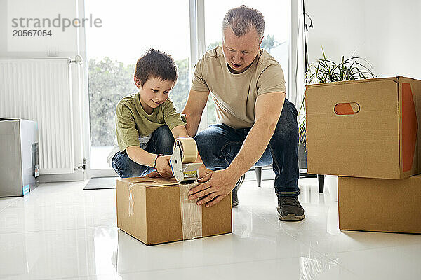 Father and son packing cardboard box with tape at home