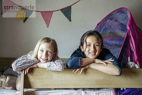 Smiling girls leaning on bunk bed at home