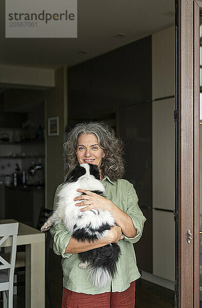 Happy mature woman carrying dog and standing in doorway