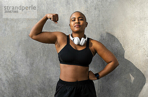 Confident sporty woman flexing muscles in front of wall