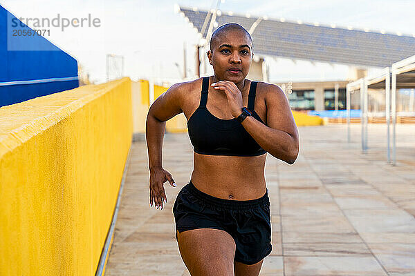 Muscular bald woman running near yellow wall