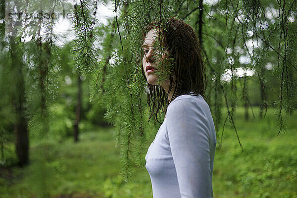 Young woman standing between wet leaves in forest