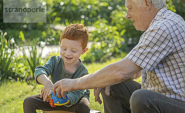 Happy grandfather and grandson playing with toy car on sunny day in back yard