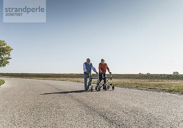 Senior friends holding mobility walker and walking at country road