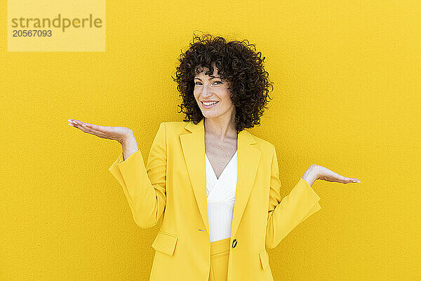 Smiling beautiful woman wearing blazer gesturing in front of yellow wall