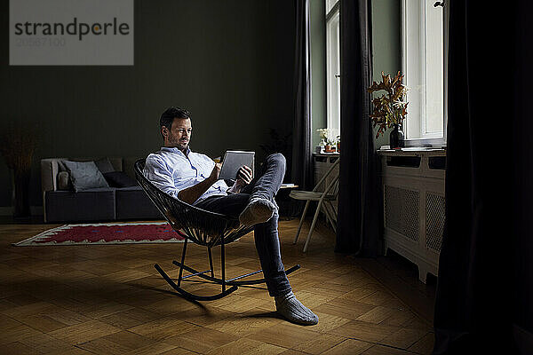 Man sitting on rocking chair and using tablet PC at home