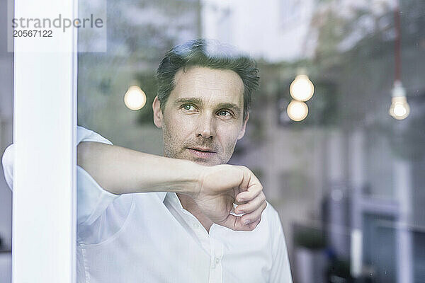 Thoughtful handsome mature businessman looking out through office window