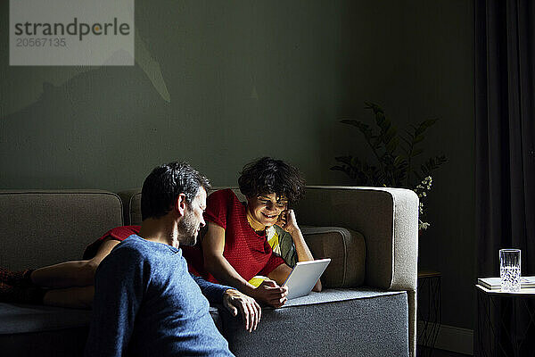 Happy woman lying on sofa and using tablet PC with boyfriend at home