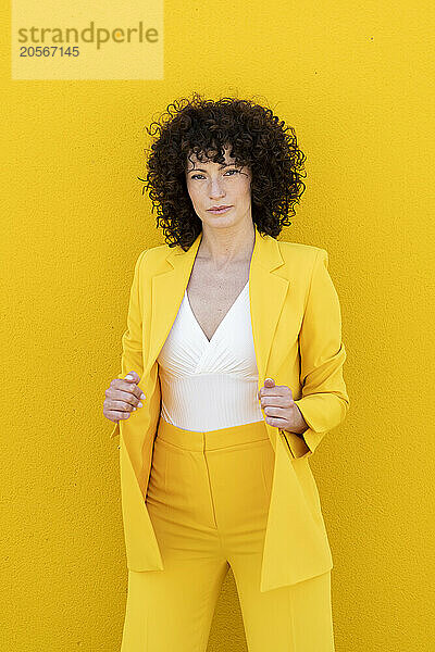 Confident woman wearing blazer standing in front of yellow wall