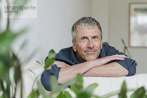 Smiling retired man resting head on arms at home