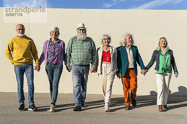 Retired women and men holding hands walking in front of wall on sunny day