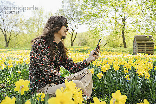 Man using smart phone sitting in flower meadow