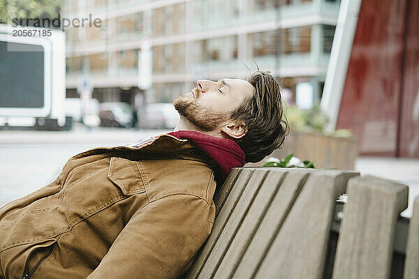 Handsome man with eyes closed resting on bench at street