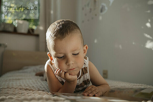 Cute boy on bed reading picture book at home