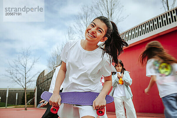 Cheerful teenage girl with skateboard at playground