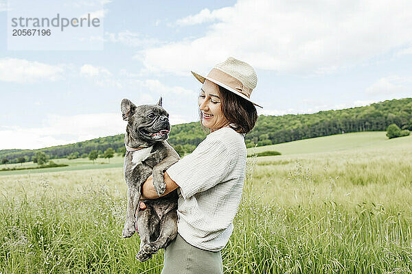 Cheerful woman carrying french bulldog in field