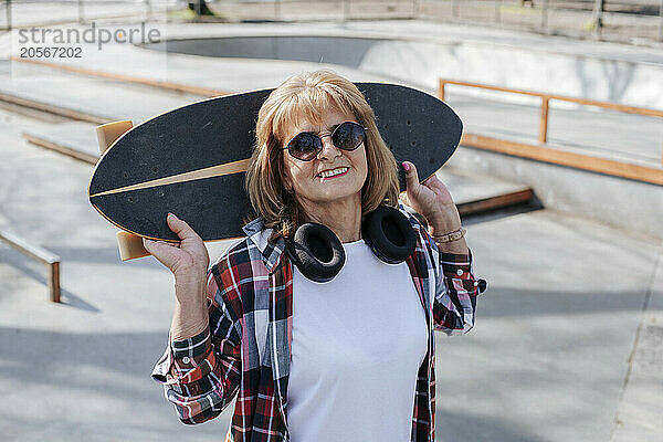 Happy woman carrying skateboard on shoulders on sports ramp in park