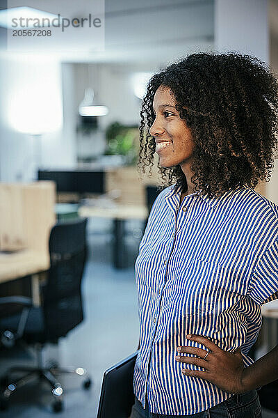 Smiling curly hair woman standing with hand on hip at cafe