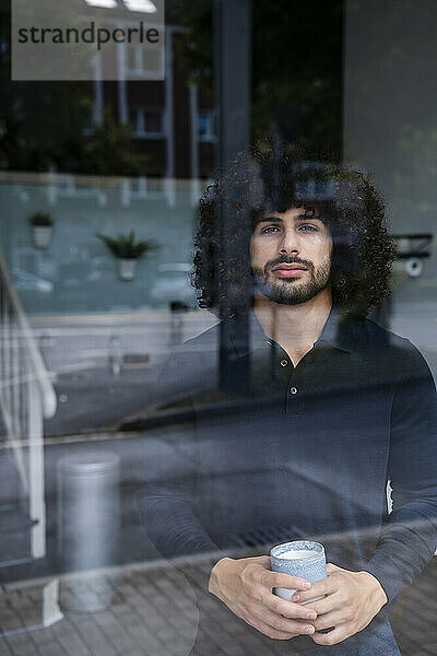 Confident businessman with coffee cup looking out through window