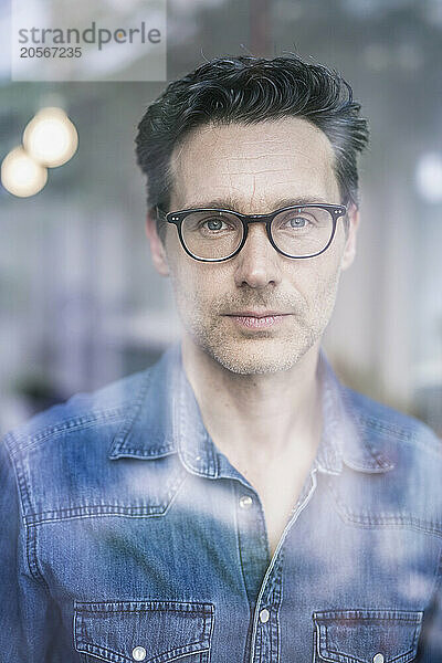 Confident businessman wearing eyeglasses looking out through office window