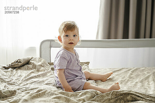 Cute toddler girl sitting on bed at home