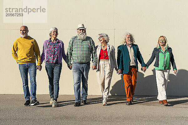 Retired men and women holding hands walking in front of wall on sunny day