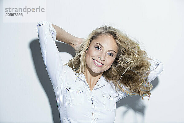 Smiling woman with hands behind head against white background