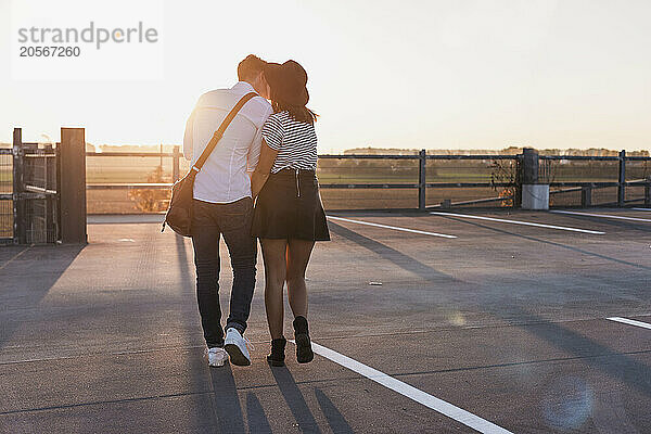 Affectionate woman kissing boyfriend on parking lot at sunrise