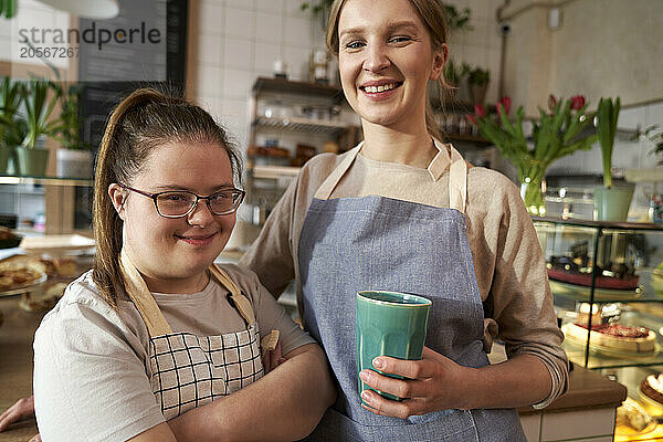 Happy coffee shop owner with down syndrome standing by colleague in cafe