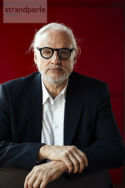 Confident senior businessman wearing eyeglasses in front of red wall