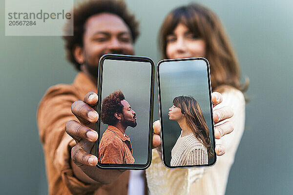 Multiracial couple showing selfie on smart phones against gray background