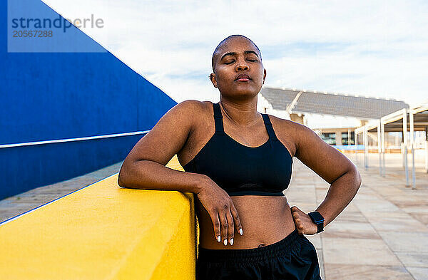 Bald woman standing with eyes closed near wall